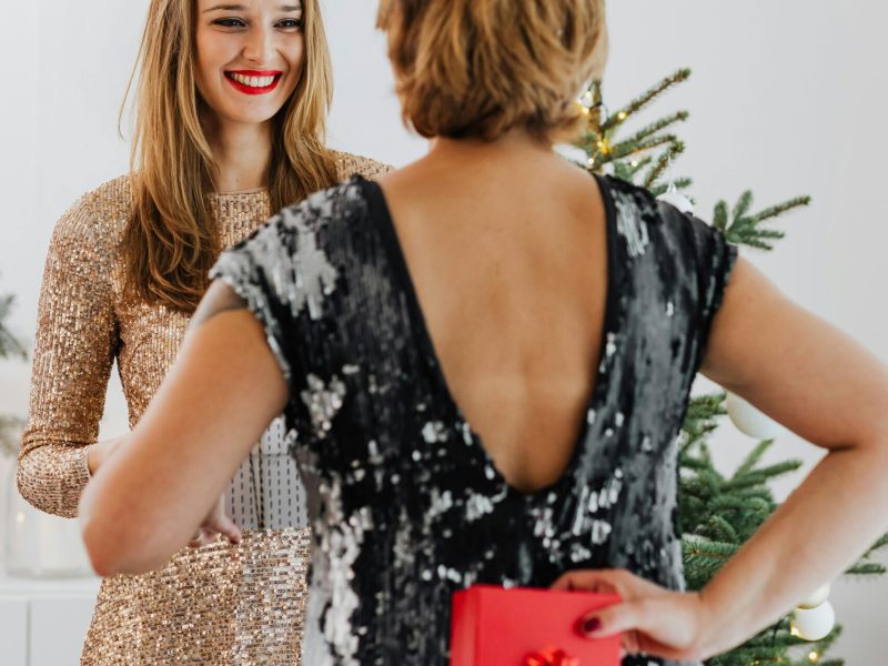 Two women exchanging gifts during a cheerful holiday celebration indoors.